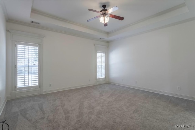 carpeted spare room featuring a tray ceiling, visible vents, crown molding, and ceiling fan