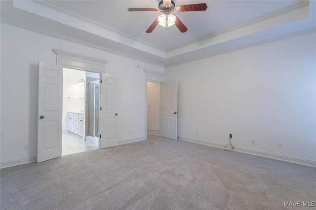 empty room with a tray ceiling, crown molding, light colored carpet, a ceiling fan, and baseboards