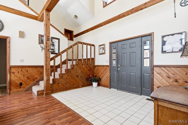 entryway featuring stairway, a wainscoted wall, high vaulted ceiling, and wooden walls