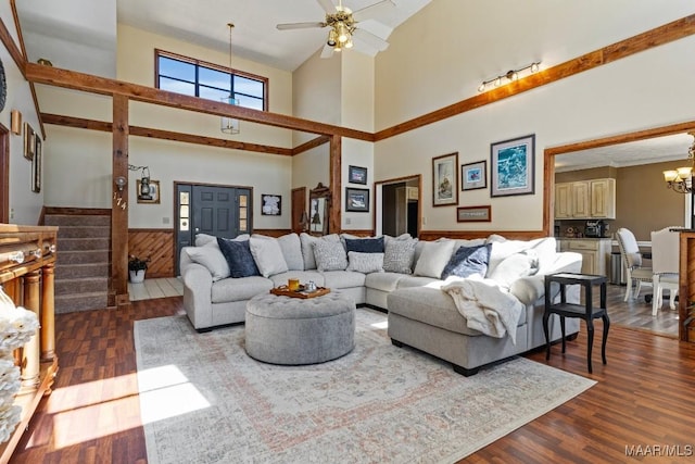 living area featuring wooden walls, wainscoting, stairway, wood finished floors, and ceiling fan with notable chandelier