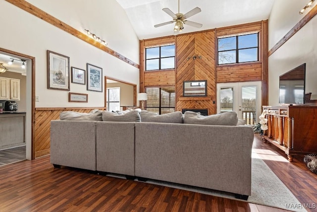 living area featuring wainscoting, a towering ceiling, ceiling fan, dark wood-style flooring, and wood walls