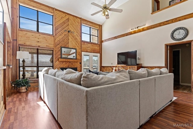 living area featuring ceiling fan, high vaulted ceiling, a wainscoted wall, dark wood-type flooring, and wood walls