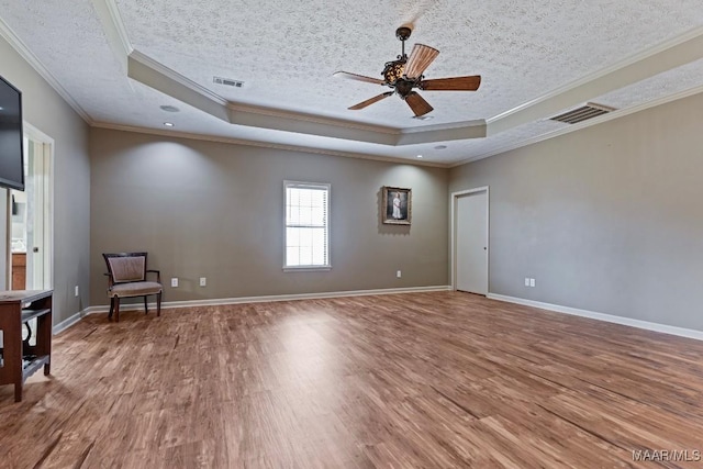 unfurnished room with a tray ceiling, wood finished floors, and visible vents