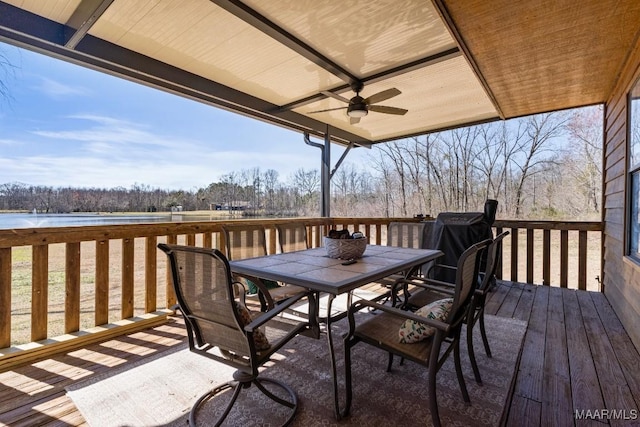 wooden terrace with a ceiling fan, outdoor dining space, and a water view