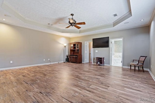 unfurnished living room featuring a textured ceiling, wood finished floors, visible vents, baseboards, and a tray ceiling