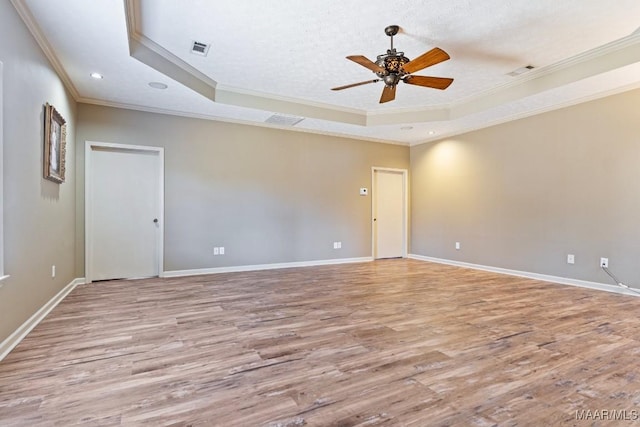 spare room featuring light wood-type flooring, a raised ceiling, and baseboards