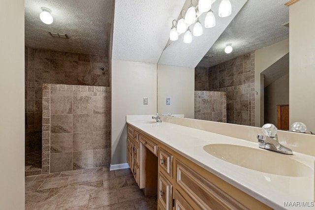 full bath featuring double vanity, a sink, a textured ceiling, and walk in shower