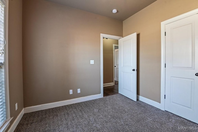 unfurnished bedroom featuring dark carpet and baseboards