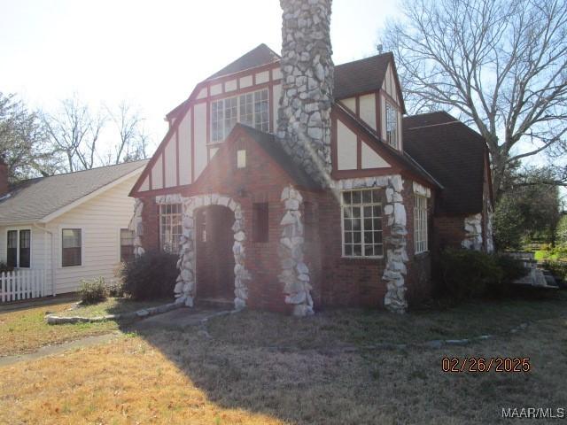 tudor house with stone siding, a chimney, and a front yard