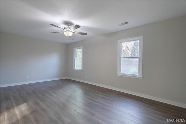 spare room with a ceiling fan, visible vents, dark wood finished floors, and baseboards