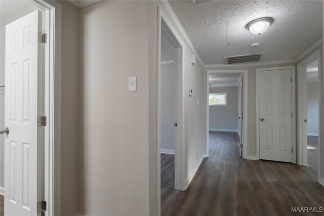 hall with dark wood-style flooring, visible vents, a textured ceiling, and baseboards