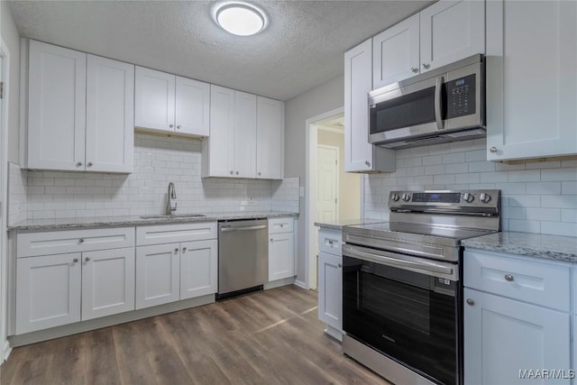 kitchen with appliances with stainless steel finishes, white cabinets, a sink, and dark wood-style floors