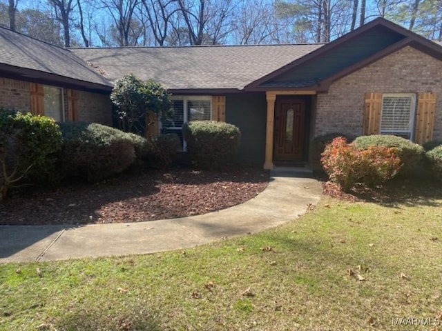 view of front facade featuring a shingled roof, brick siding, and a front lawn