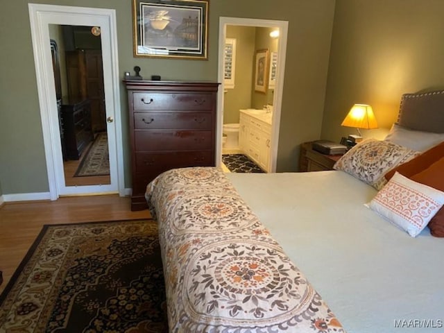 bedroom with baseboards, wood finished floors, and ensuite bathroom