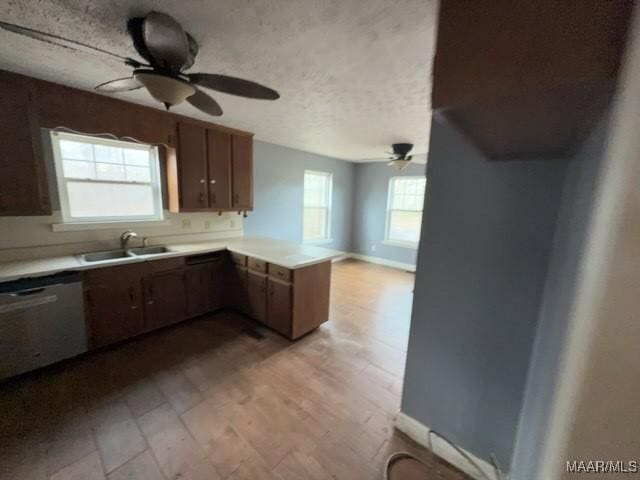 kitchen featuring light countertops, stainless steel dishwasher, a ceiling fan, a sink, and a peninsula