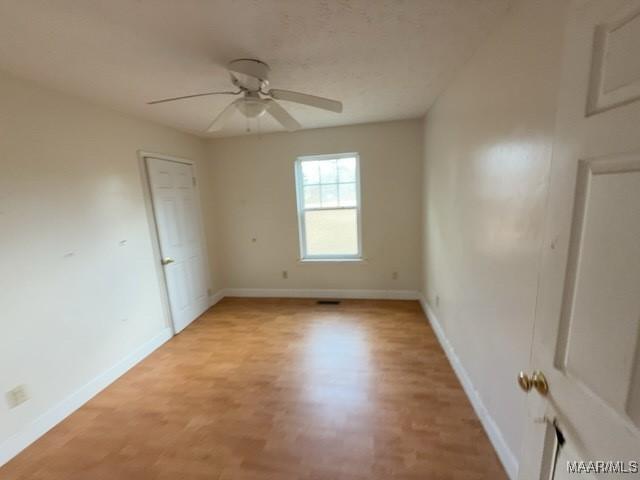 empty room featuring light wood-type flooring, a ceiling fan, and baseboards