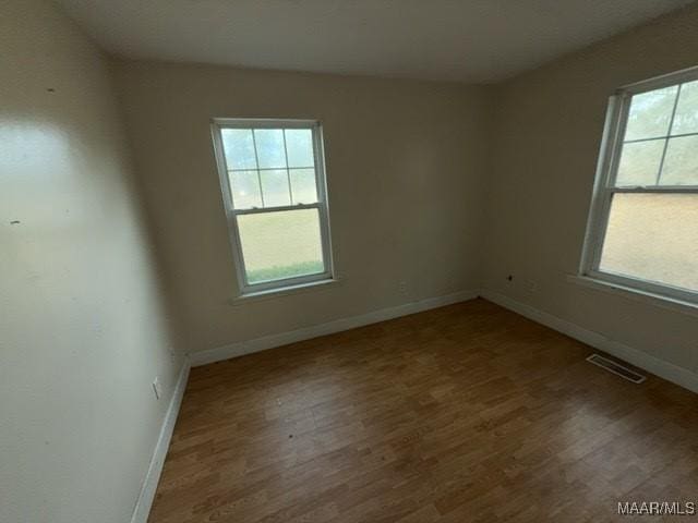 unfurnished room with a healthy amount of sunlight, visible vents, and wood finished floors