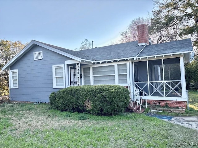 view of front of house featuring a chimney, a front yard, and a sunroom