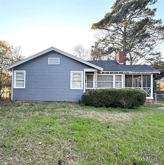 view of front facade featuring a sunroom, a chimney, and a front yard