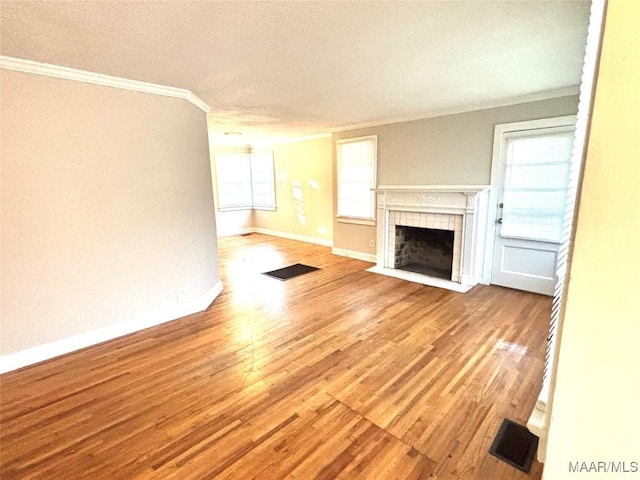 unfurnished living room with wood finished floors, visible vents, baseboards, a tiled fireplace, and crown molding