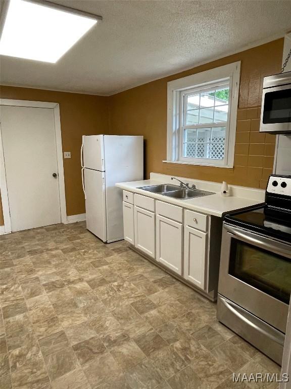 kitchen with stainless steel appliances, a textured ceiling, light countertops, white cabinetry, and a sink