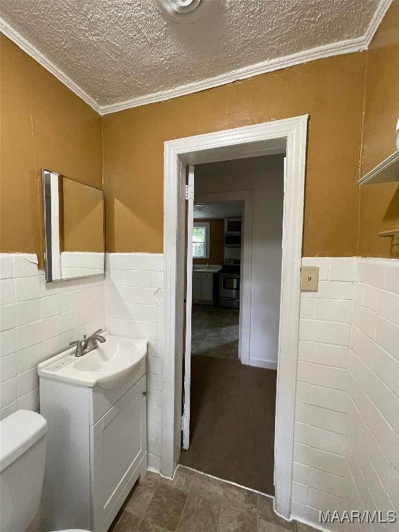 bathroom with toilet, a wainscoted wall, ornamental molding, and a textured ceiling