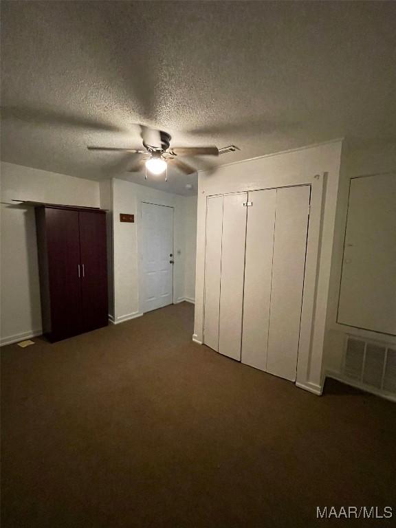 unfurnished bedroom with visible vents, a ceiling fan, a textured ceiling, dark carpet, and multiple closets