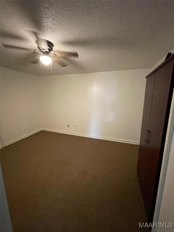 unfurnished room with a ceiling fan, dark colored carpet, and baseboards