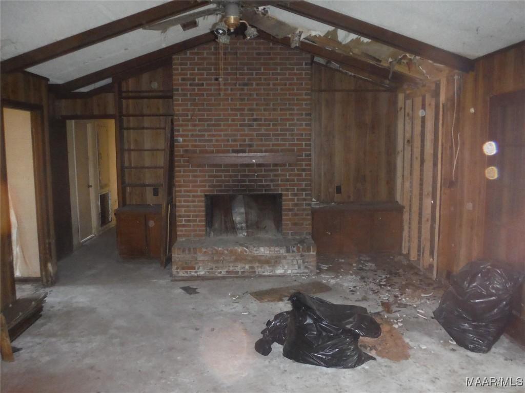 unfurnished living room featuring vaulted ceiling with beams, wood walls, and a brick fireplace