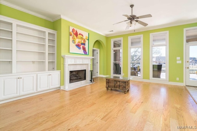 unfurnished living room with ceiling fan, light wood-type flooring, crown molding, and a tile fireplace