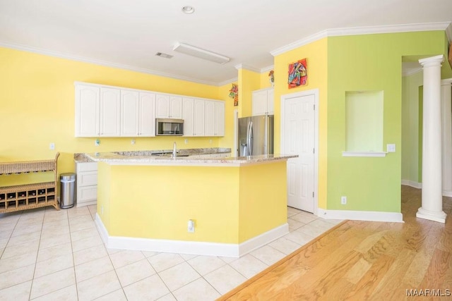 kitchen with a kitchen island with sink, stainless steel appliances, crown molding, ornate columns, and white cabinetry