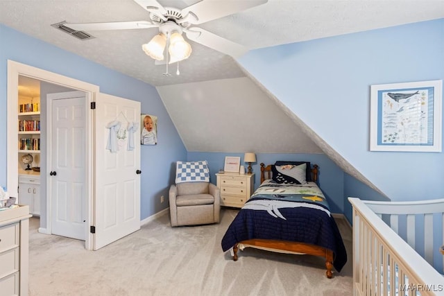 bedroom with visible vents, vaulted ceiling, a textured ceiling, and light colored carpet