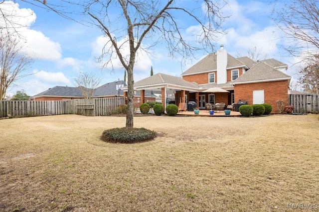 rear view of house featuring fence private yard, a chimney, brick siding, and a yard