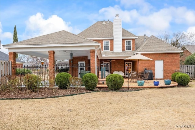 back of house featuring brick siding, fence, roof with shingles, a chimney, and a patio area