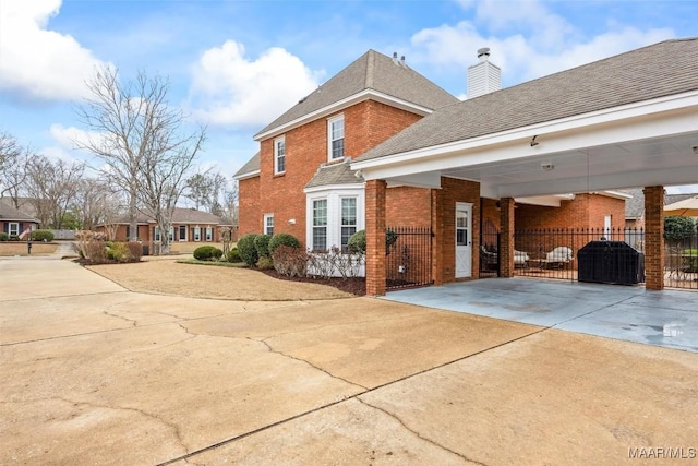 view of front of house featuring brick siding, a chimney, a shingled roof, concrete driveway, and fence