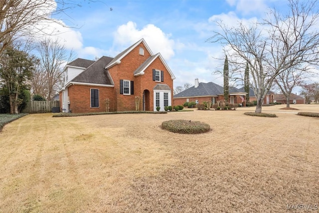 traditional home featuring fence, a front lawn, and brick siding