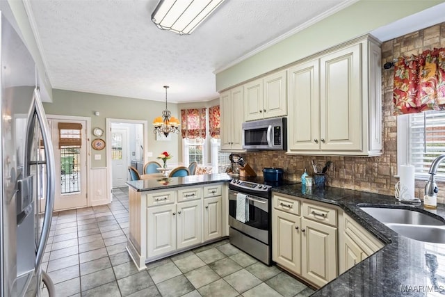 kitchen featuring a notable chandelier, stainless steel appliances, cream cabinets, a sink, and a peninsula