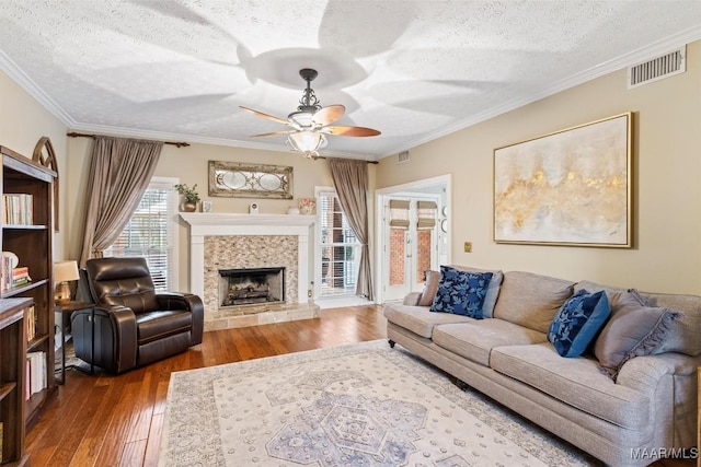 living room featuring crown molding, visible vents, a tiled fireplace, a textured ceiling, and hardwood / wood-style floors