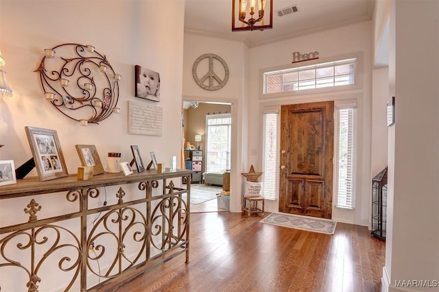 entryway with a chandelier, a high ceiling, wood finished floors, visible vents, and crown molding