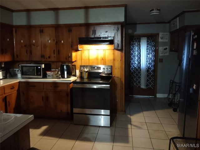 kitchen featuring light tile patterned floors, under cabinet range hood, light countertops, appliances with stainless steel finishes, and brown cabinetry