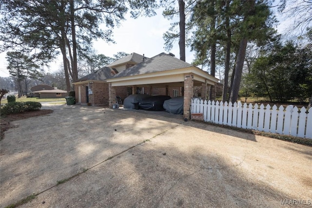 view of property exterior with driveway, brick siding, and fence