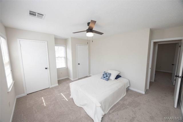 bedroom featuring light carpet, a ceiling fan, multiple closets, visible vents, and baseboards