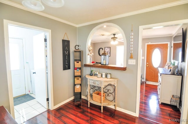 hallway featuring arched walkways, crown molding, baseboards, and wood finished floors