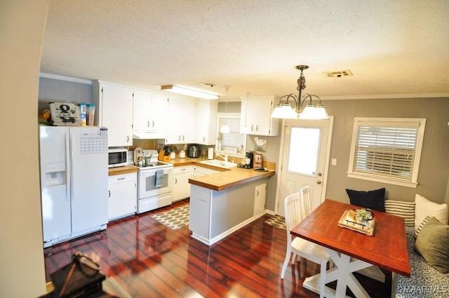 kitchen with a peninsula, white appliances, dark wood-type flooring, a sink, and visible vents