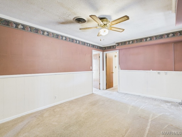 spare room with visible vents, wainscoting, ceiling fan, a textured ceiling, and carpet flooring