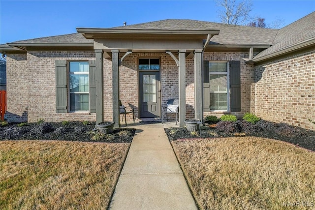 doorway to property featuring brick siding and a shingled roof