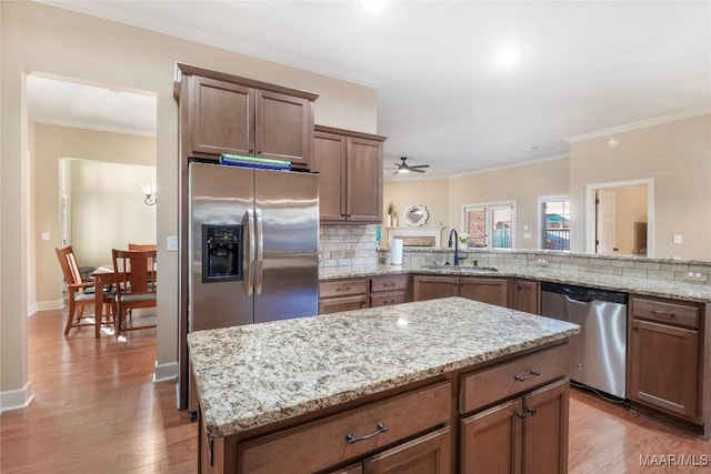 kitchen featuring stainless steel appliances, a sink, light wood-type flooring, decorative backsplash, and crown molding