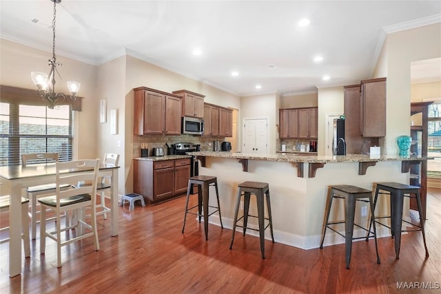 kitchen with stainless steel appliances, a peninsula, wood finished floors, a kitchen breakfast bar, and tasteful backsplash