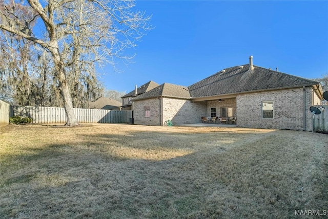 rear view of property with brick siding, a lawn, and fence