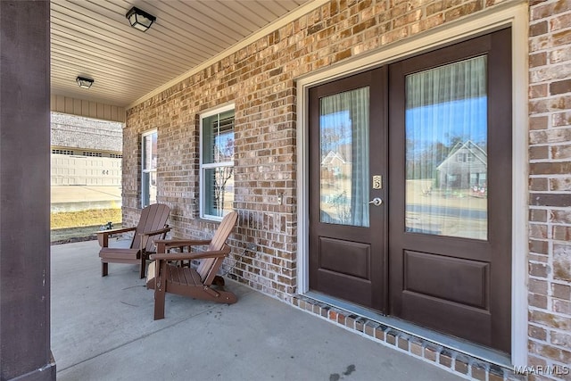 property entrance with a porch, french doors, and brick siding